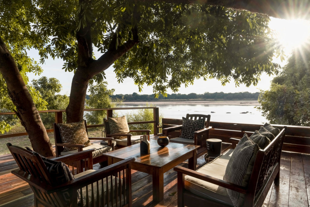 Cushioned wooden chairs gather beneath a shady tree on a riverside deck, the wide sandbanks of the Luangwa glinting in the late afternoon sun.