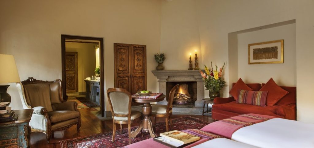 Colonial suite with a stone fireplace, carved wooden armoire and a red velvet sofa beside an antique dining table