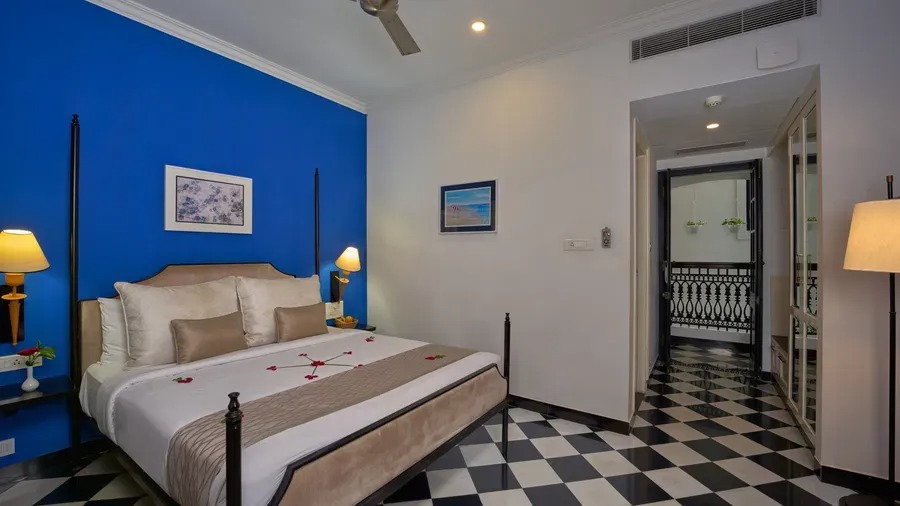 A Boutique Room bedroom at The Old Court House with a bold blue accent wall, four-poster-style bed and black-and-white checkered flooring, opening onto a balcony.