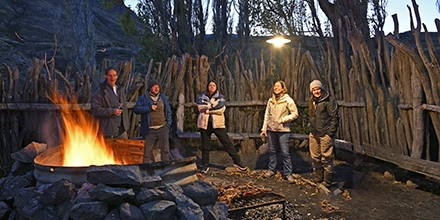 Group of people standing around a large open fire in a rustic wooden enclosure at Estancia El Cóndor.