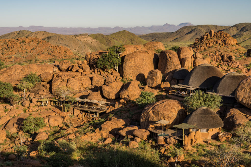 An elevated view over Mowani Mountain Camp shows its thatched suites and pool deck woven through a maze of ancient granite boulders.