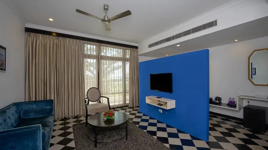 A Heritage Classic Room seating area featuring a wall-mounted television, cream armchair and round coffee table set against checkered flooring.