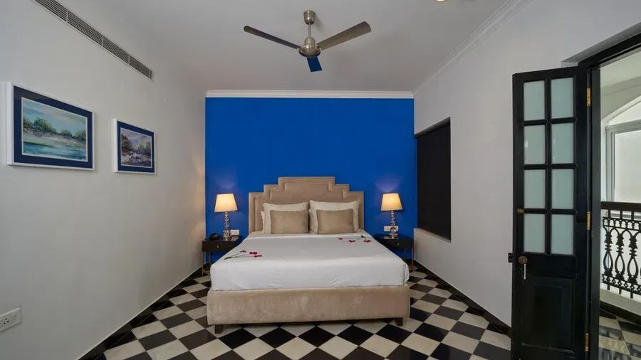 Heritage Classic bedroom in Fort Kochi with a deep blue feature wall, upholstered headboard and open door leading to a private balcony.