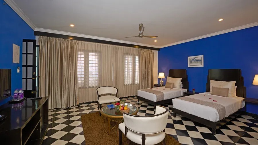 A twin-bed Heritage Classic Room with vivid blue walls, plush drapery and cream armchairs arranged around a coffee table.