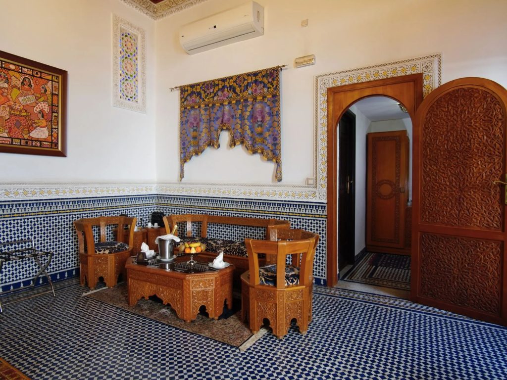 A sitting corner with blue and white zellige tiling, an embroidered wall hanging and a carved cedar door.