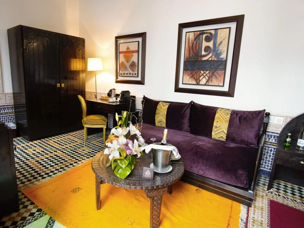 A sitting nook with a plum velvet sofa, geometric black and white tiled floor and a golden-yellow rug.