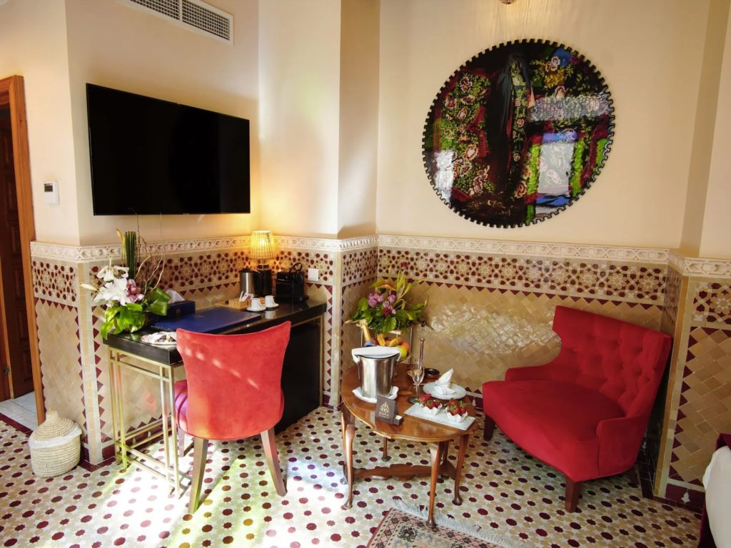 A seating corner with a round patterned artwork on the wall, a tufted red armchair and a small work desk.