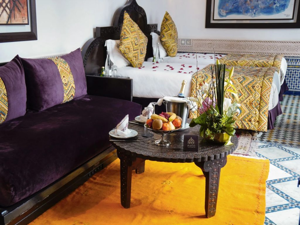 Twin beds dressed in gold patterned linens, scattered with rose petals, beside a plum velvet sofa.