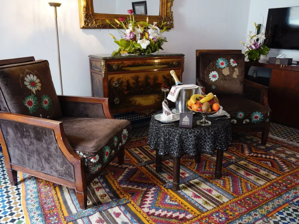 A pair of embroidered velvet armchairs beneath a gilt-framed mirror, set on a richly patterned Berber rug.