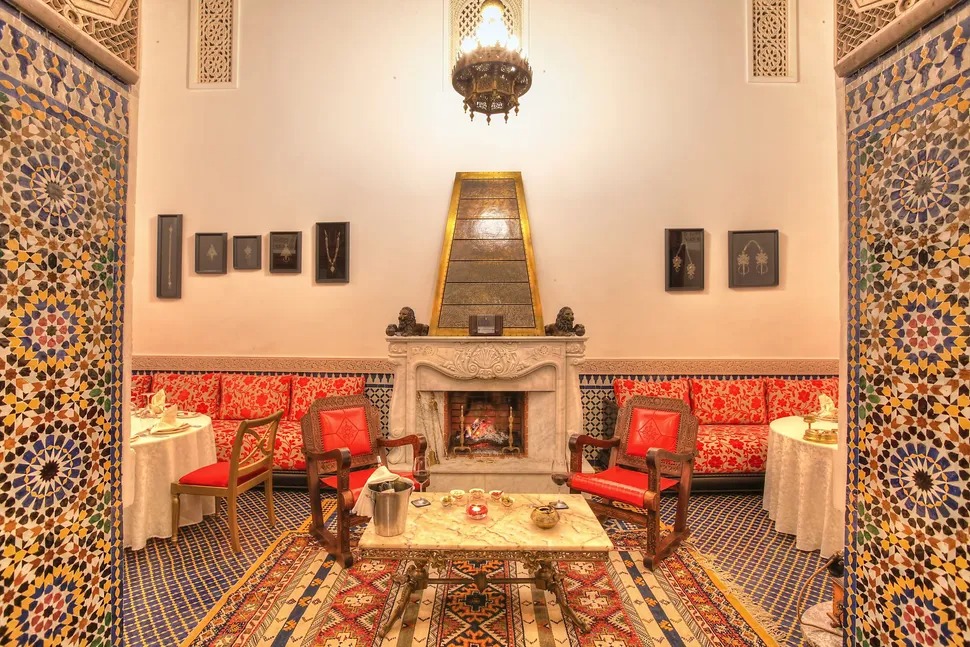 A fireside lounge with red upholstered seating and tiled archways in traditional Fassi style.