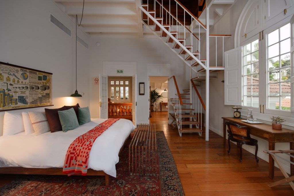 Split-level suite with a white staircase, antique writing desk and a bed dressed in white linen with a woven throw