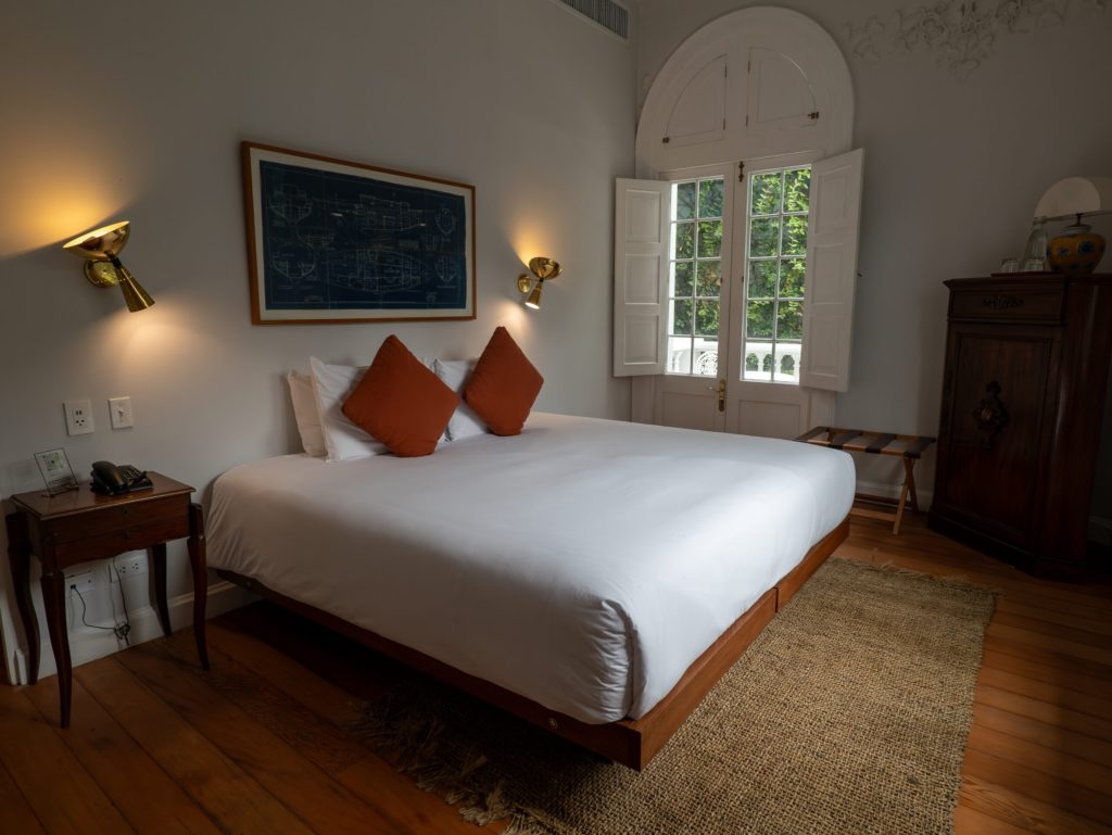Bedroom with a framed nautical blueprint above the bed, brass wall sconces and arched shuttered doors opening to a balcony