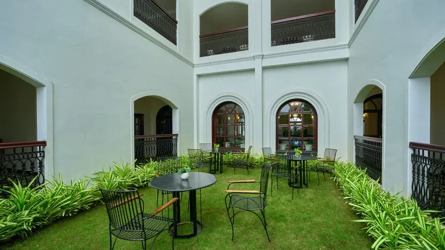 A tranquil courtyard garden with café-style seating, manicured lawns and arched colonial windows.