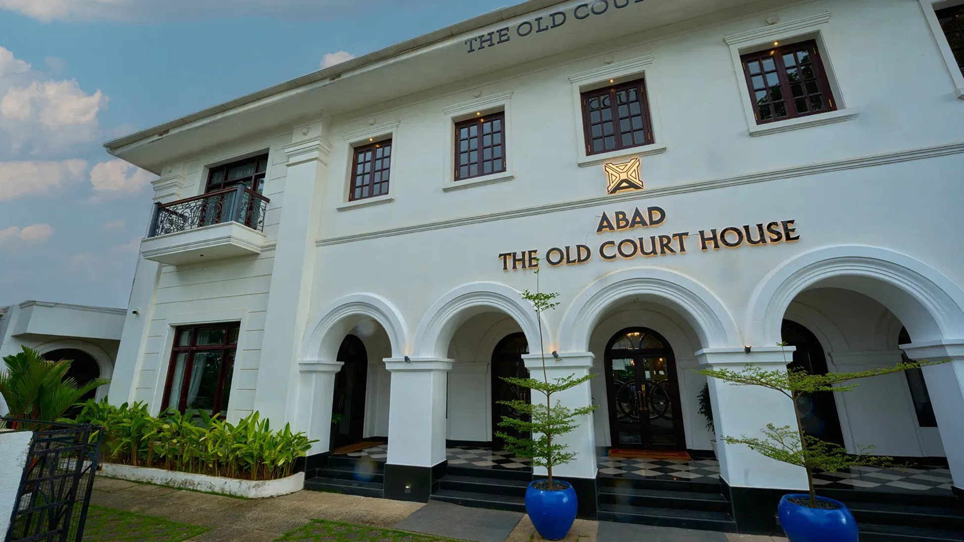 An angled view of the hotel's colonial facade in Fort Kochi, showcasing its symmetrical windows and arched ground-floor entrance.