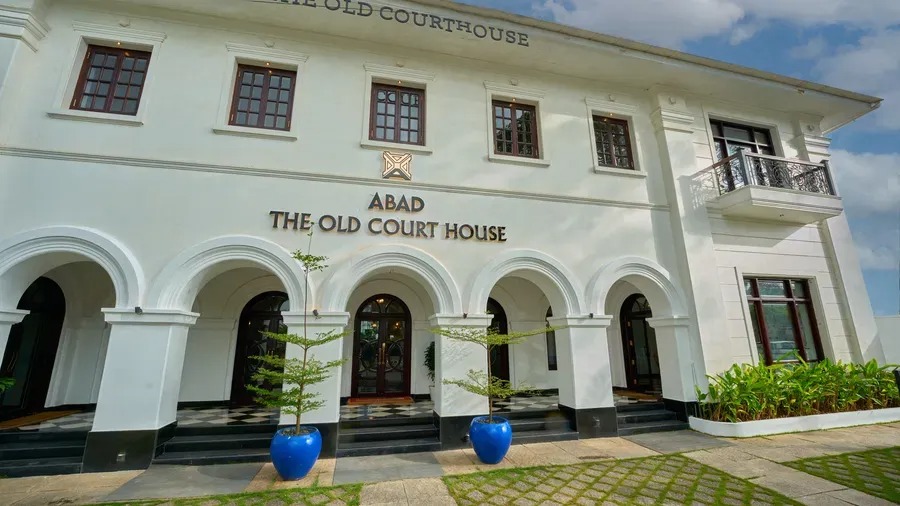 Wide-angle daytime view of the hotel exterior, with landscaped gardens and blue planters framing the entrance steps.