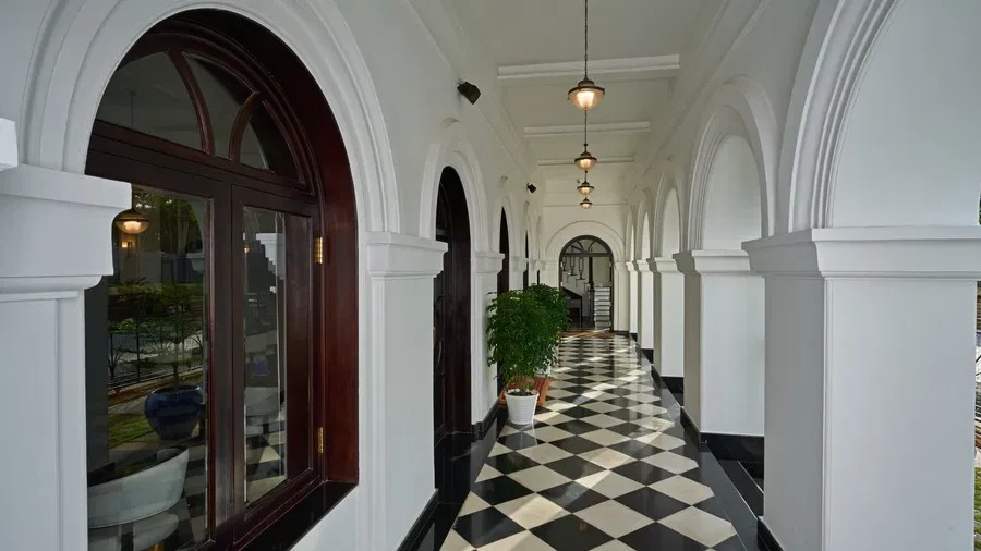 An elegant arched corridor with pendant lighting and checkered flooring, leading toward the hotel's interior.