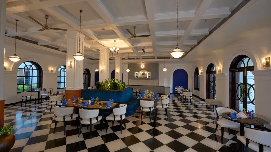 The hotel's dining hall with a coffered ceiling, pendant lights and blue-accented booth seating over checkered floors.