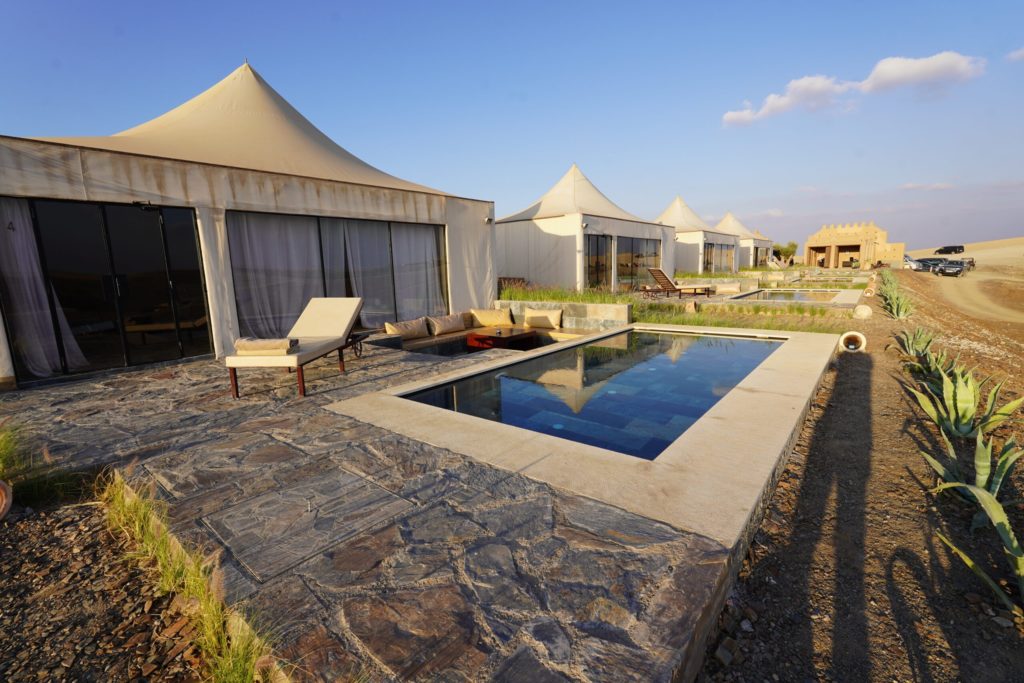 Rows of canvas lodges and private pools stretch across the Agafay landscape, a kasbah-style building in the distance.