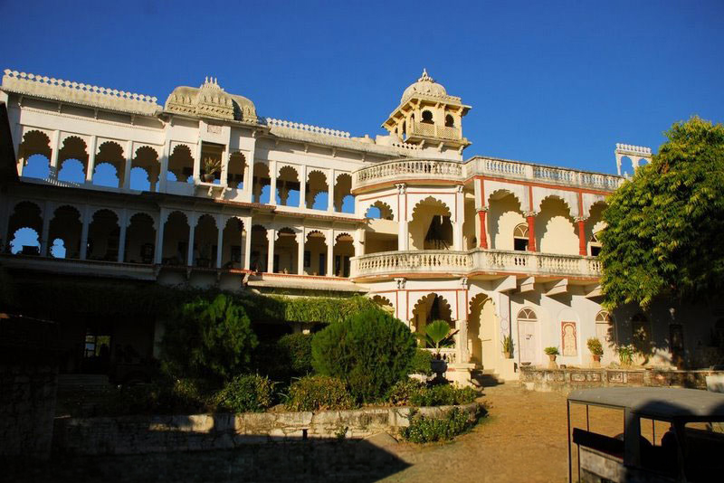 The layered arcaded courtyard of Darbargadh Poshina, with domed towers, red-trimmed balconies and gardens framing the fort's entrance
