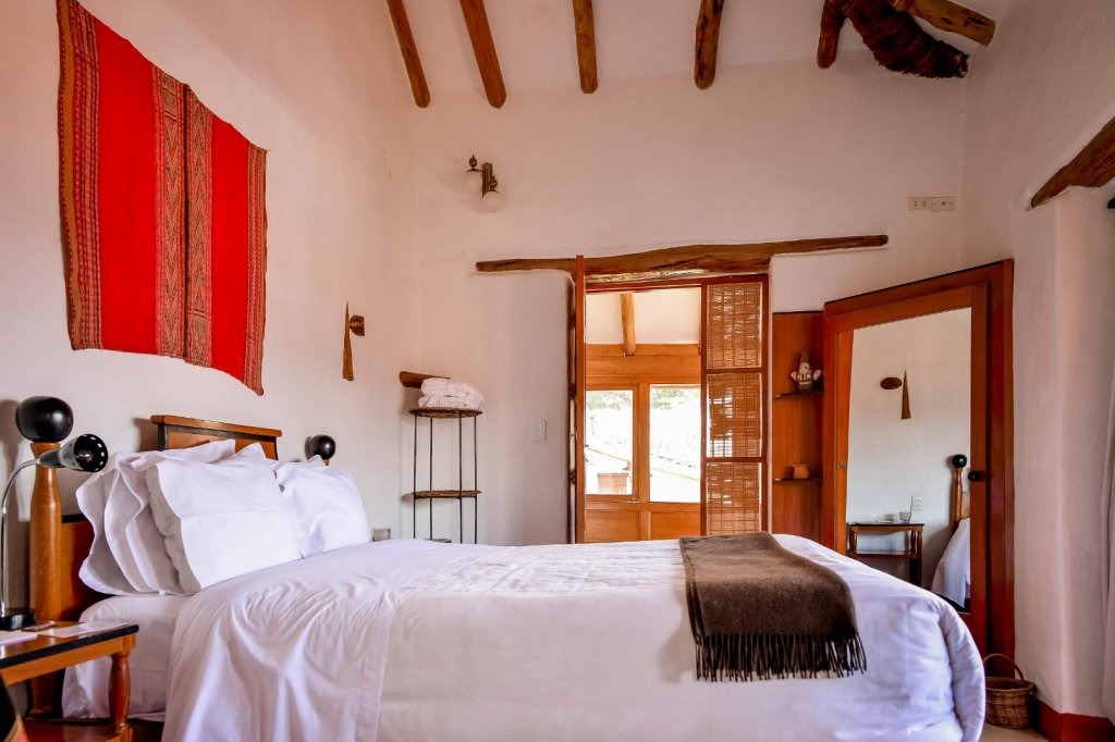 Rustic bedroom with a red woven Andean textile above the bed and a wood-framed door opening to a balcony