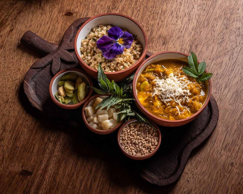 Rustic wooden platter of Andean farm-to-table dishes, including barley, broad beans and choclo corn