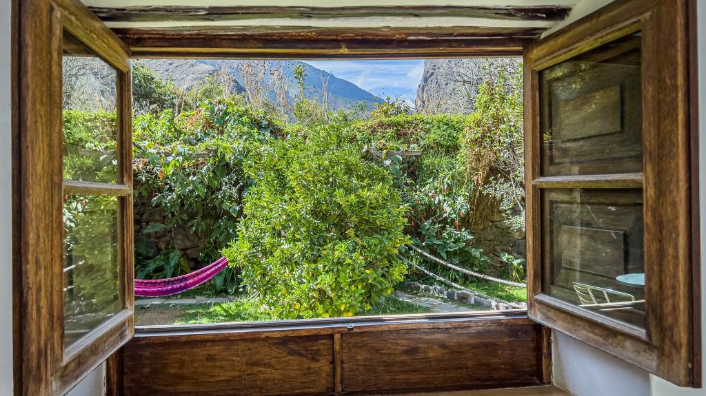 Open wooden shutters framing a garden view with a hammock strung beneath flowering shrubs