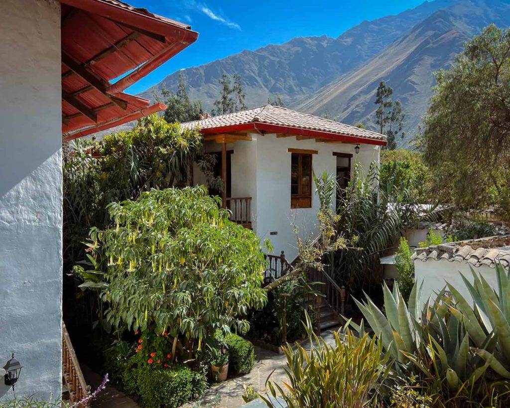 Whitewashed cottage with tiled roof set among agave and flowering trees against mountain views