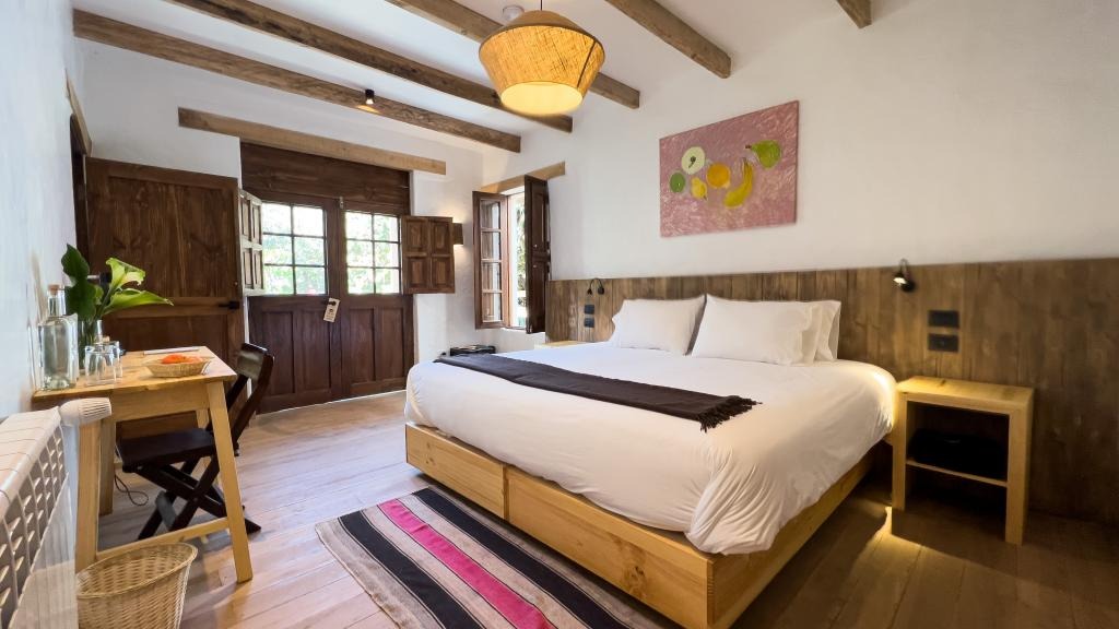 Beamed bedroom with king bed, striped rug and writing desk beside open wooden doors