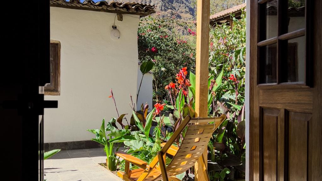 Wooden chairs on a garden terrace beside blooming canna lilies and a view towards the mountains