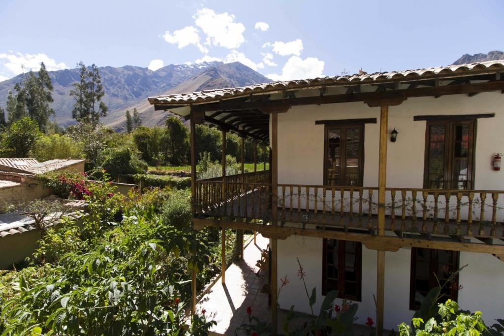 Two-storey hotel building with wraparound balcony overlooking gardens and the Sacred Valley peaks