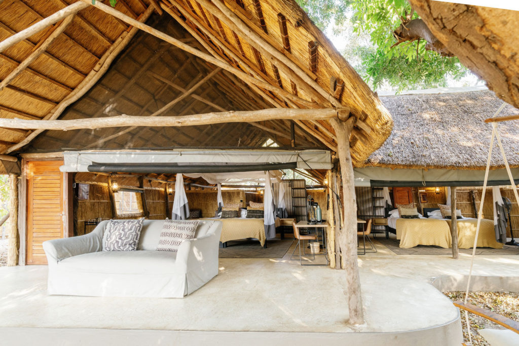 The family safari room's open-plan layout unfolds beneath soaring thatch, a soft sofa and twin canopy beds arranged beneath a canvas roof.