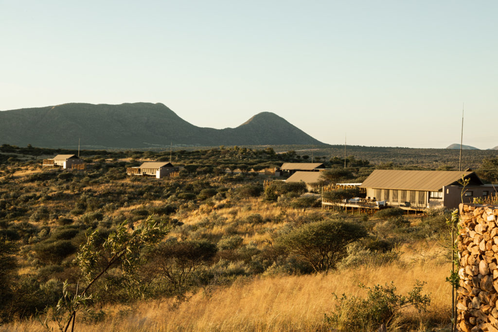 Aerial view of the lodge's canvas-roofed suites scattered across the Namibian savannah at sunset