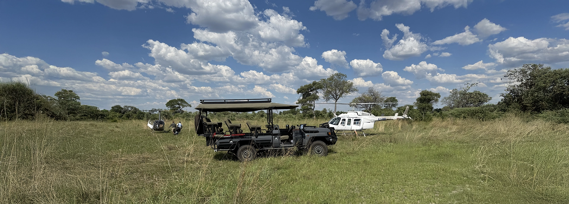 Safari vehicles and helicopters stand ready on an open grass airstrip, showcasing seamless travel through Botswana’s remote landscapes.
