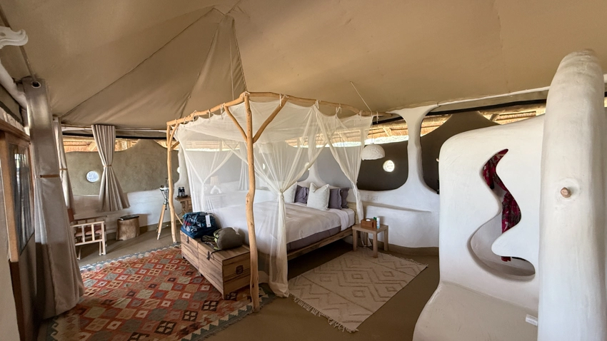An elegant safari suite features a four-poster bed draped in mosquito netting, with organic textures and sculpted walls creating a calm retreat. 