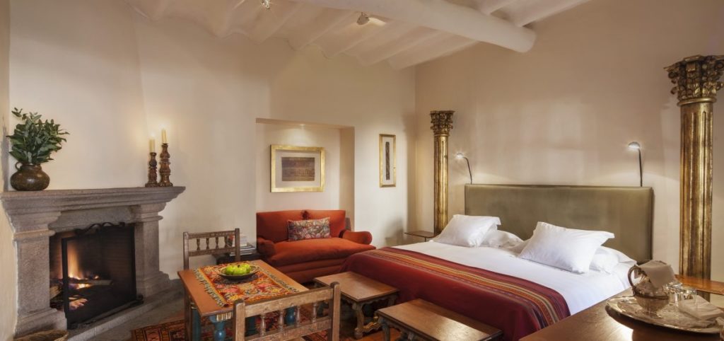 Suite with a stone fireplace, gilded columns and a bed dressed in striped Andean textiles