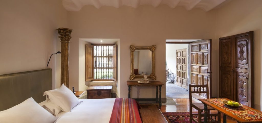 Bedroom opening onto a barred window and carved wooden doors, with a gilt-framed mirror and antique console table