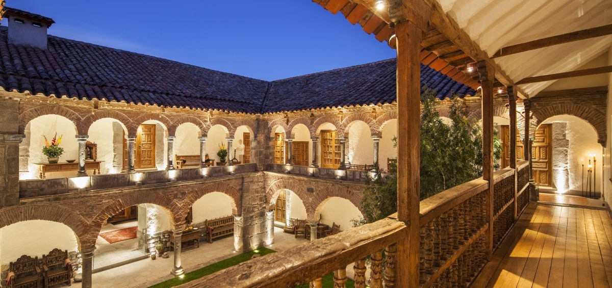 Elevated view of an arched stone cloister with wooden balustrades, carved doors and warm lantern lighting