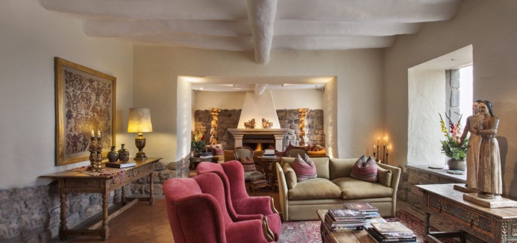 Sitting room with crimson wingback chairs, a stone fireplace niche and carved wooden santos on display