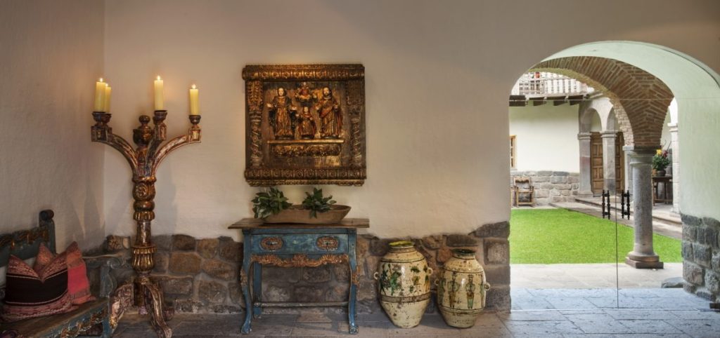 Colonial hallway with a gilded santos relief, blue painted console table and an archway opening onto the courtyard