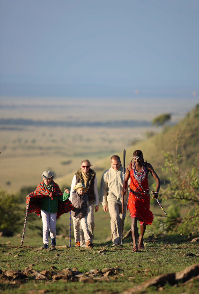 A family and their Maasai guide walk the escarpment trail overlooking the Masai Mara plains