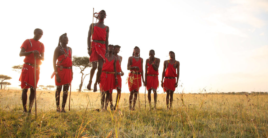 Maasai performers in red shuka gather in the golden grass for a traditional jumping dance at sunset