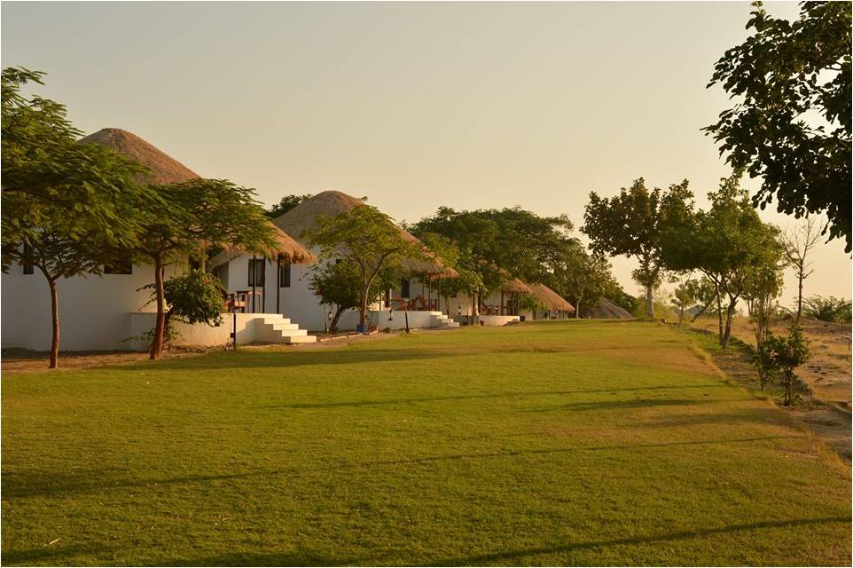 Thatched-roof cottages set along a lawn at Kutch Safari Resort, Bhuj