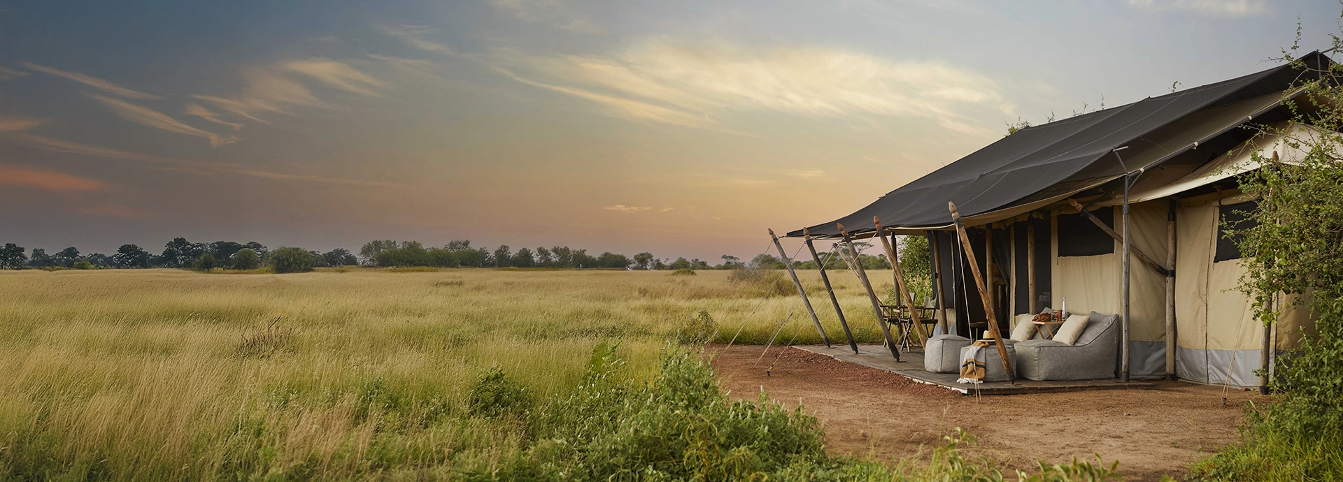 The exterior of a classic safari tent sits lightly on the plains, with canvas walls and a shaded deck overlooking wide Serengeti vistas.