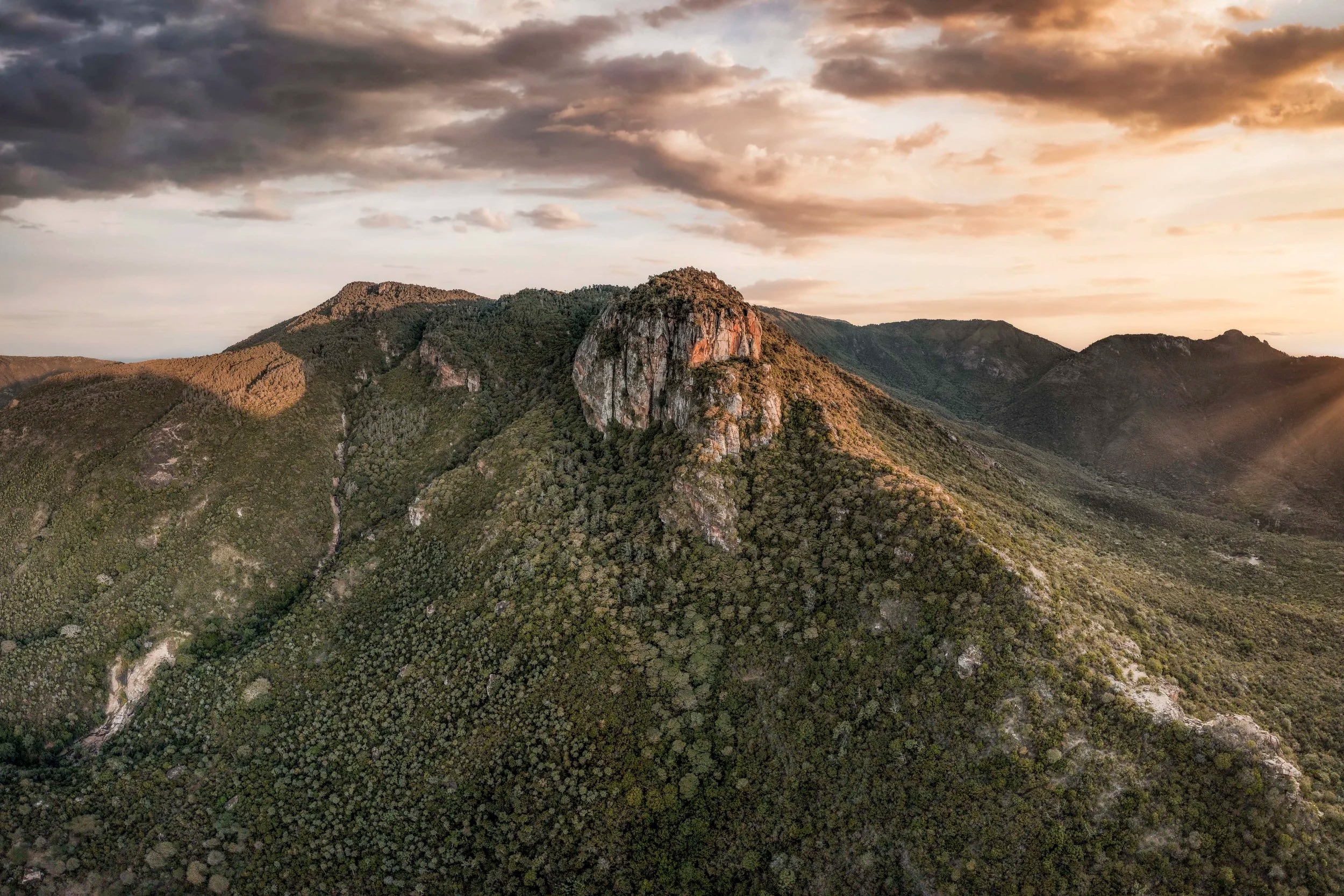 Aerial view of a rocky outcrop on the forested slopes of Mount Nyiru, northern Kenya, lit by low sunset light under broken cloud.