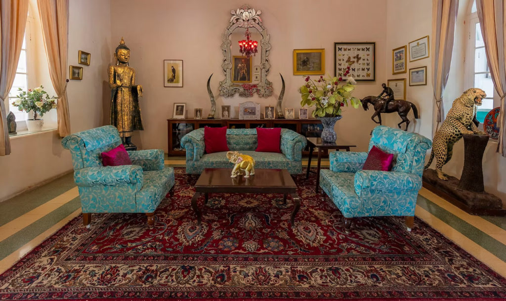 A sitting room at Orchard Palace, Gondal, furnished with turquoise sofas, hunting trophies and a gilded Buddha statue