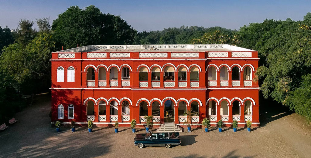 An aerial view of Orchard Palace's arched red fa&ccedil;ade, framed by mango and lime trees