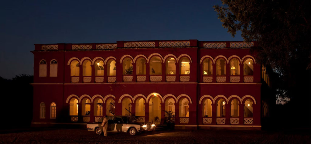 Orchard Palace lit up at dusk, with a vintage car waiting beneath its arched verandas