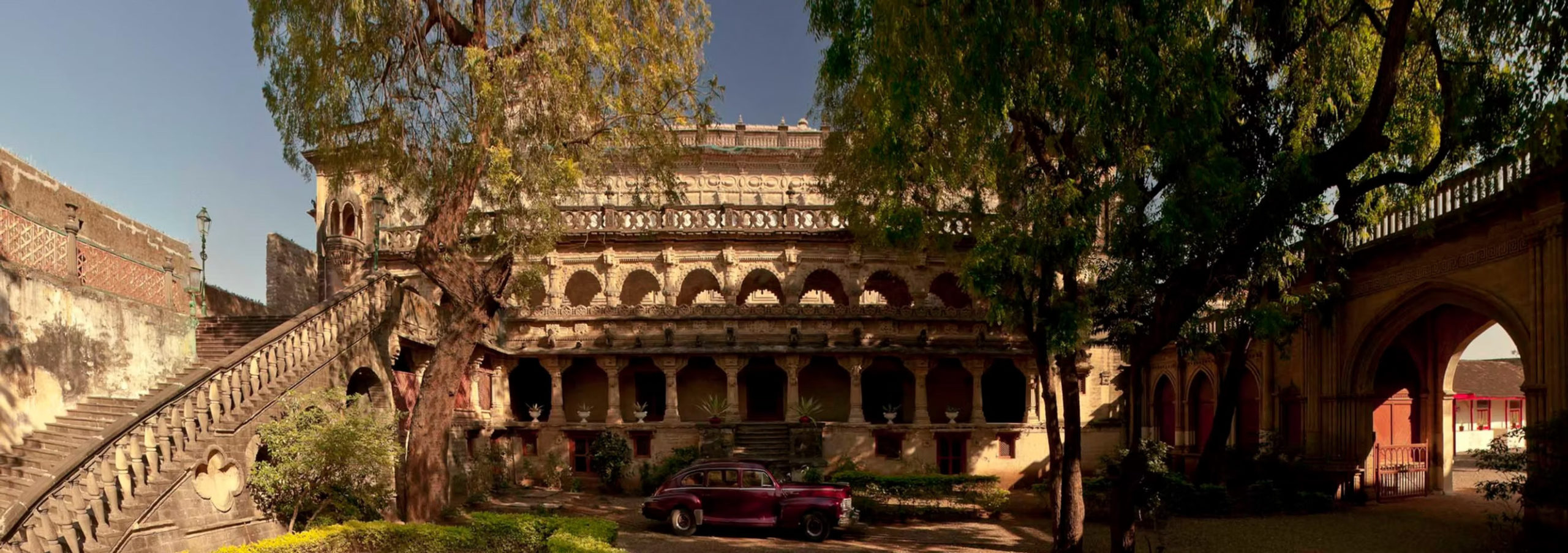 A vintage maroon car parked beneath the ornately carved balconies of the historic Gondal palace