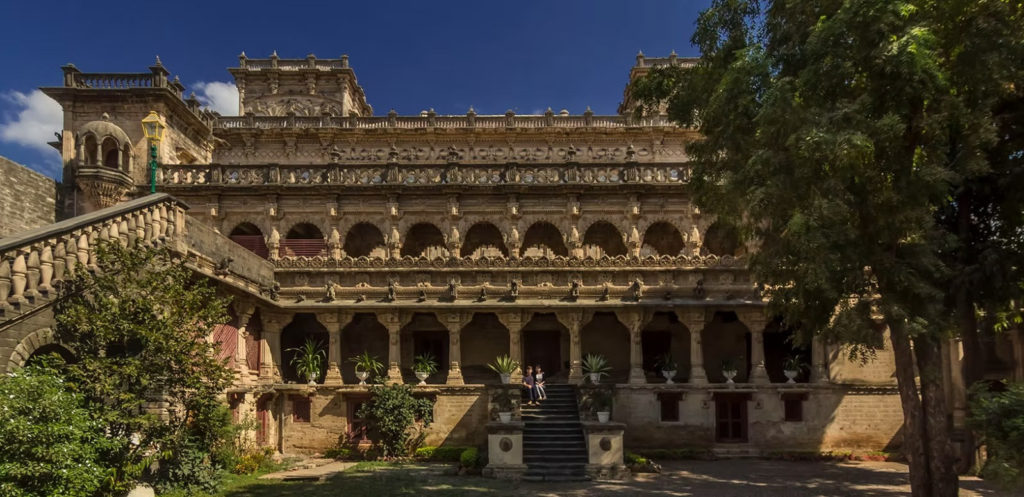 Guests sit on the steps of a richly carved stone palace building in Gondal