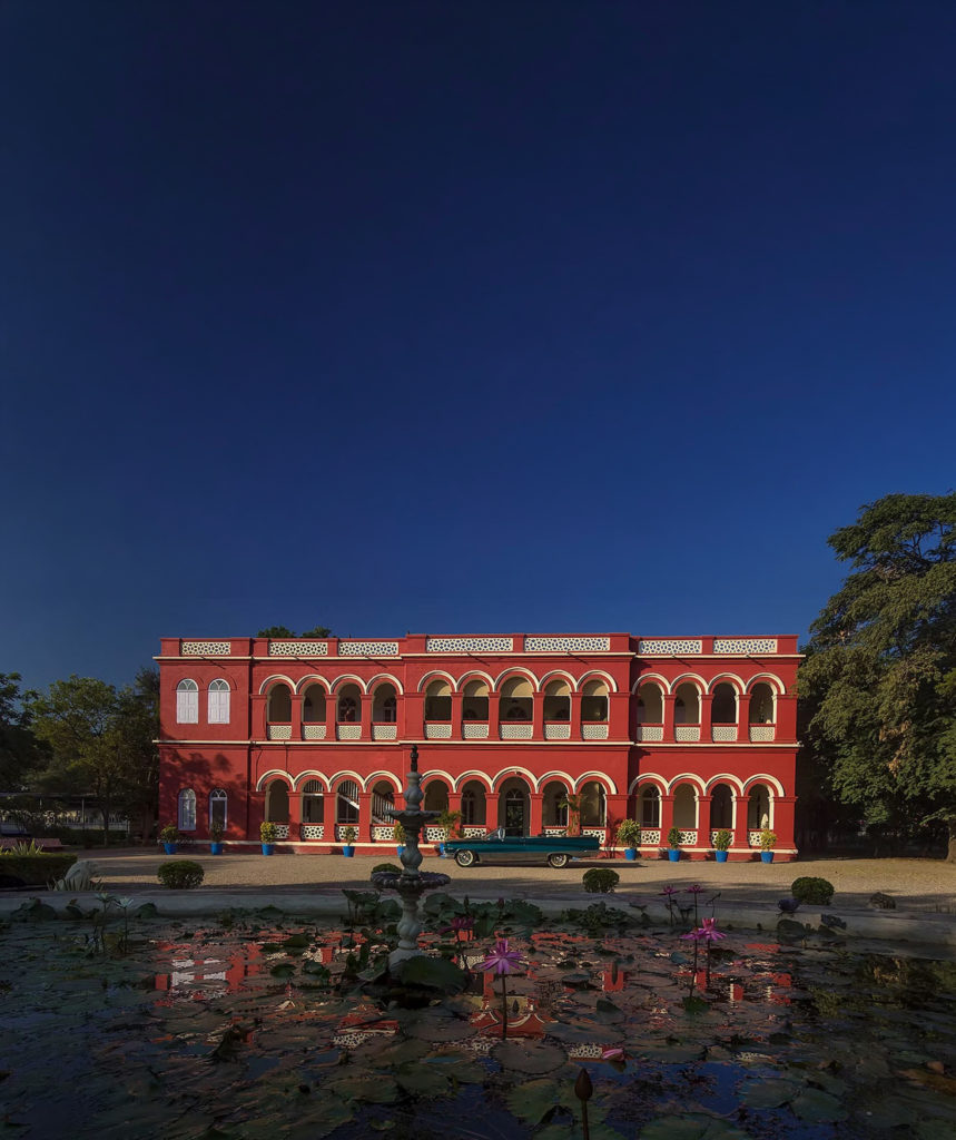 The red art deco fa&ccedil;ade of Orchard Palace, Gondal, glows at dusk beside a vintage car